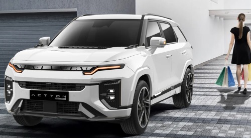 A person walking away from a KGM Actyon Hybrid, holding some shopping and going into their house.