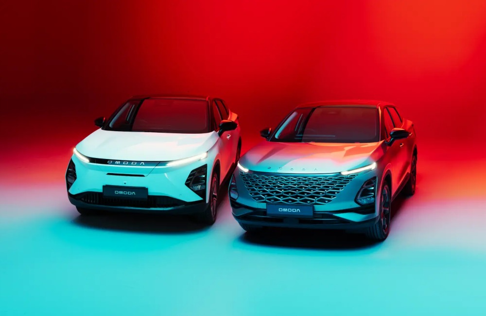 A photoshoot showing off two OMODA cars. The backdrop is red and blue. Both cars are showing off their front design and day time running lights.